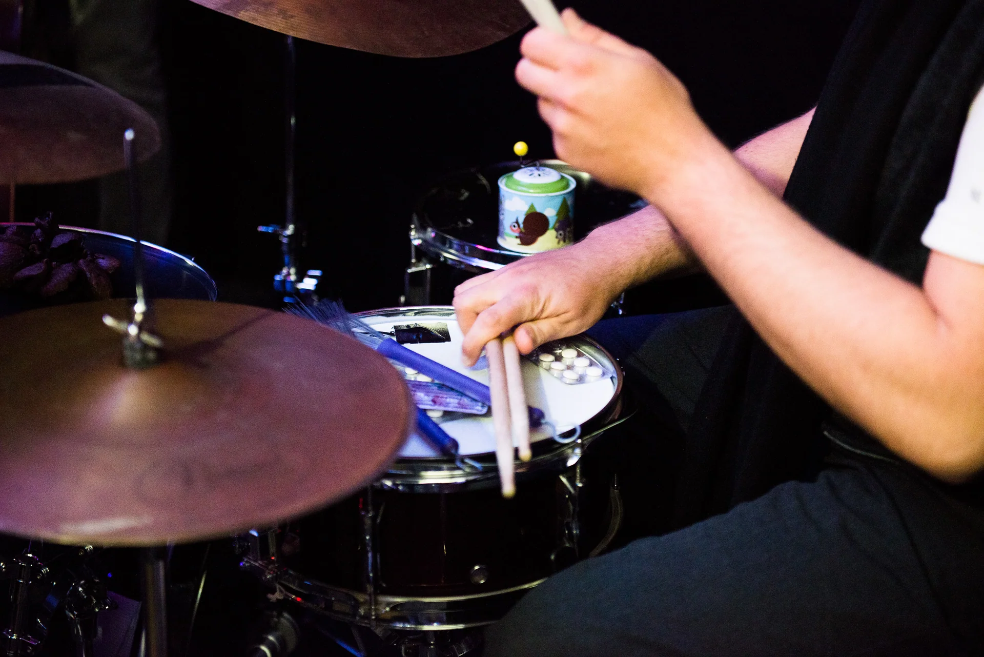 A close-up of hands, sticks and brushes at a snare drum and cymbals